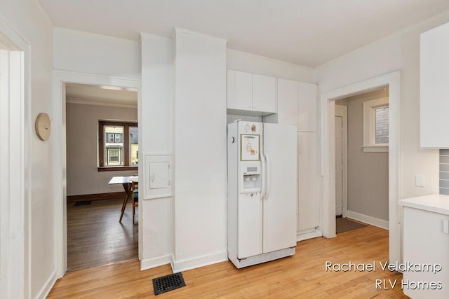 kitchen with white fridge with ice dispenser, light wood-type flooring, white cabinets, light countertops, and baseboards