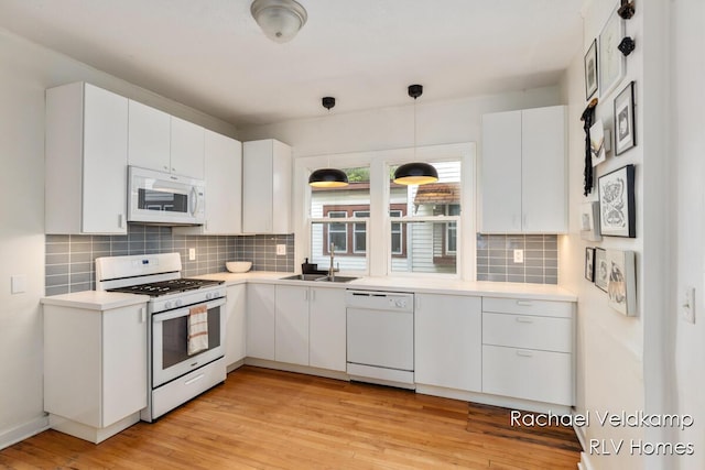 kitchen with white appliances, a sink, tasteful backsplash, light countertops, and white cabinetry