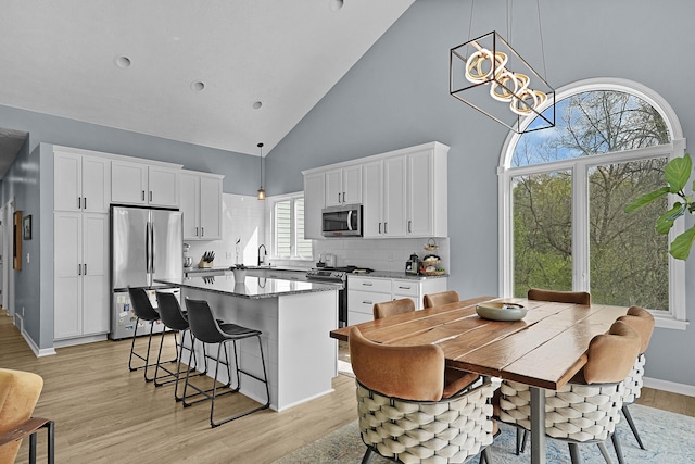 12700 Mcpherson St NE, Lowell, MI 49331 - kitchen featuring stainless steel appliances, high vaulted ceiling, white cabinetry, a breakfast bar area, and light wood finished floors
