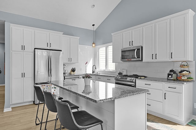 12700 Mcpherson St NE, Lowell, MI 49331 - kitchen featuring appliances with stainless steel finishes, vaulted ceiling, light stone countertops, white cabinetry, and light wood-style floors