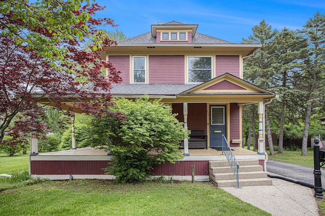 american foursquare style home with a front yard, covered porch, and a shingled roof