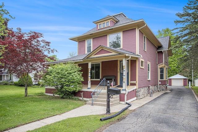 american foursquare style home featuring covered porch, a detached garage, an outbuilding, a front yard, and asphalt driveway