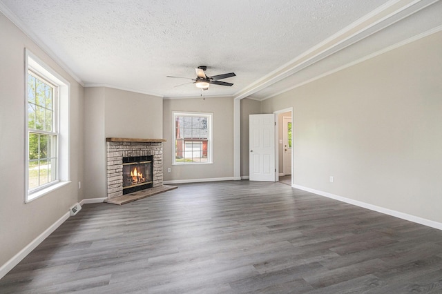 unfurnished living room featuring a textured ceiling, ceiling fan, crown molding, a brick fireplace, and dark wood-style flooring