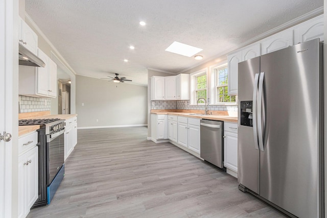 kitchen featuring appliances with stainless steel finishes, a textured ceiling, white cabinetry, butcher block counters, and baseboards