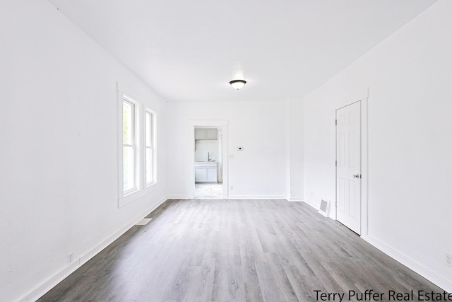 unfurnished room featuring wood finished floors, baseboards, and a sink