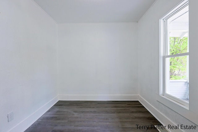 empty room featuring dark wood finished floors, baseboards, and crown molding