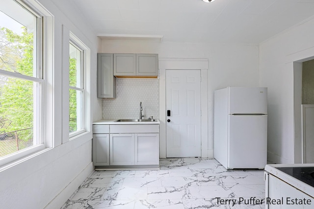 kitchen featuring white appliances, a sink, gray cabinets, light marble finish flooring, and light countertops