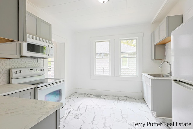 kitchen featuring white appliances, gray cabinetry, a sink, light marble finish flooring, and tasteful backsplash