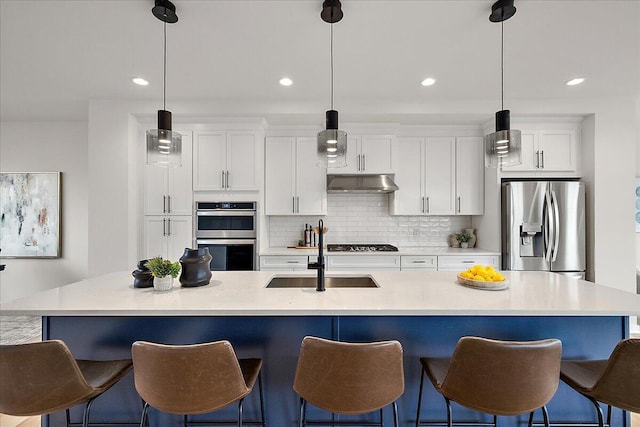 kitchen with stainless steel appliances, a sink, under cabinet range hood, white cabinets, and an island with sink