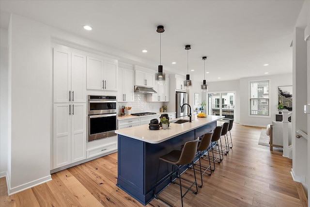 kitchen with appliances with stainless steel finishes, under cabinet range hood, an island with sink, a sink, and white cabinets