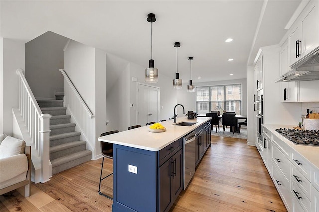 kitchen with stainless steel appliances, a kitchen bar, a sink, white cabinets, and light wood-type flooring