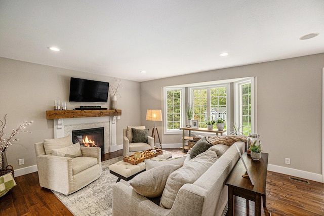 living room featuring a premium fireplace, baseboards, dark wood-type flooring, and recessed lighting