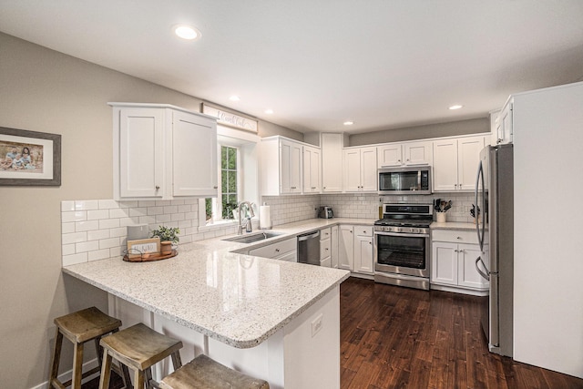 kitchen with appliances with stainless steel finishes, a sink, a peninsula, dark wood-style floors, and white cabinetry
