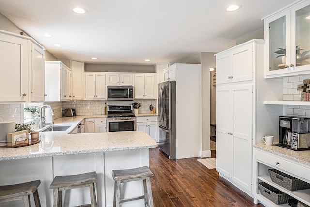 kitchen featuring stainless steel appliances, a sink, tasteful backsplash, a peninsula, and white cabinetry