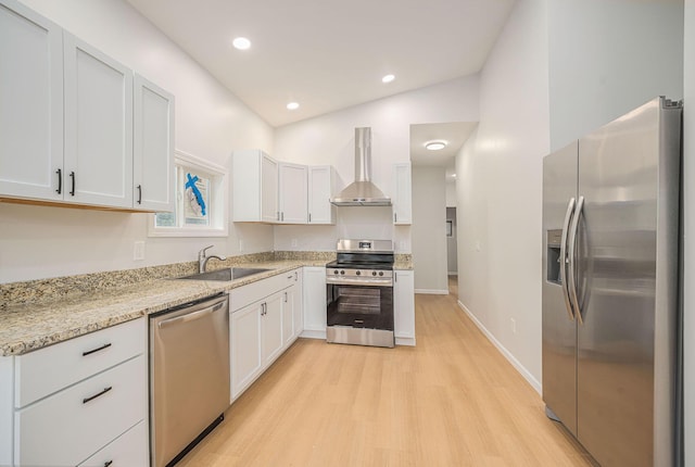 kitchen with appliances with stainless steel finishes, wall chimney exhaust hood, a sink, light wood-style floors, and light stone countertops