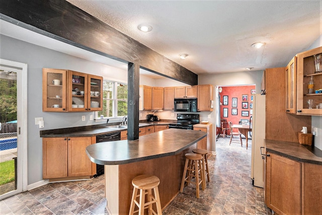 kitchen with black appliances, dark countertops, dark stone finish floors, and a kitchen breakfast bar