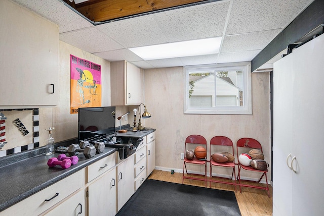 kitchen featuring a drop ceiling, light wood-style flooring, dark countertops, and baseboards