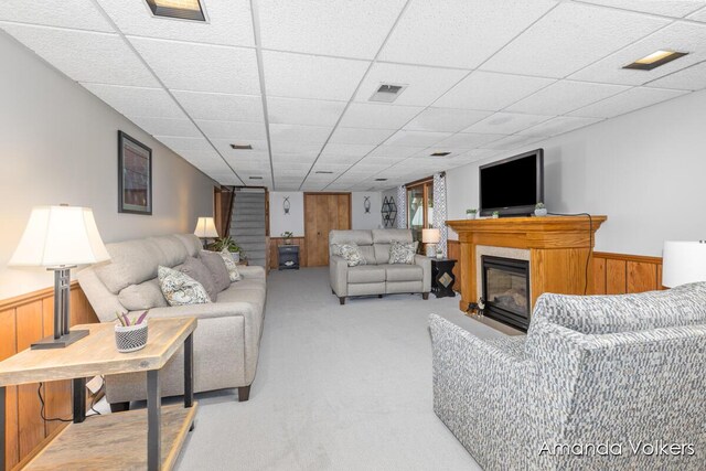 living room featuring a glass covered fireplace, carpet floors, a wainscoted wall, a drop ceiling, and wood walls