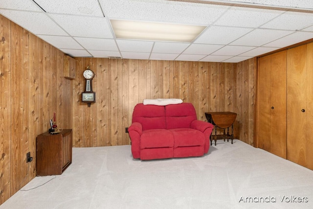 living area with carpet, a drop ceiling, and wood walls