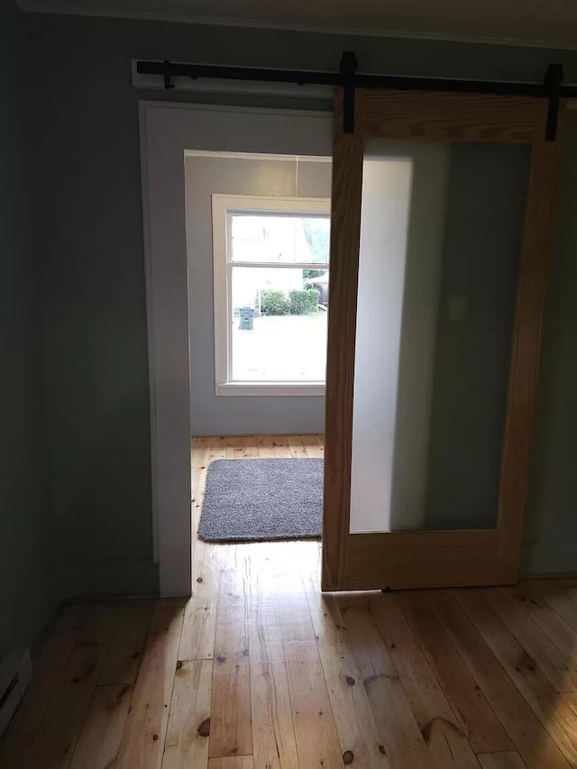 corridor with a barn door, hardwood / wood-style floors, and baseboard heating
