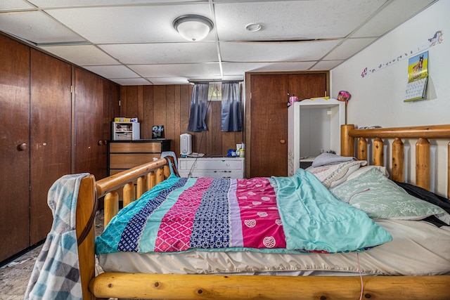 bedroom featuring a drop ceiling, a closet, and wood walls
