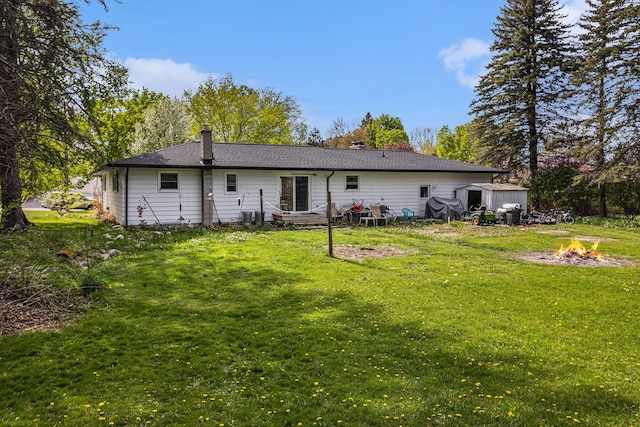 rear view of house with a fire pit, a lawn, and a chimney