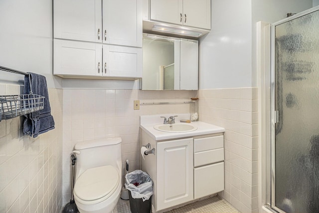 bathroom featuring tile walls, a stall shower, vanity, toilet, and wainscoting