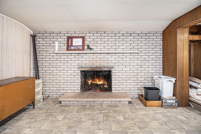 unfurnished living room with stone finish flooring, wooden walls, a brick fireplace, and brick wall