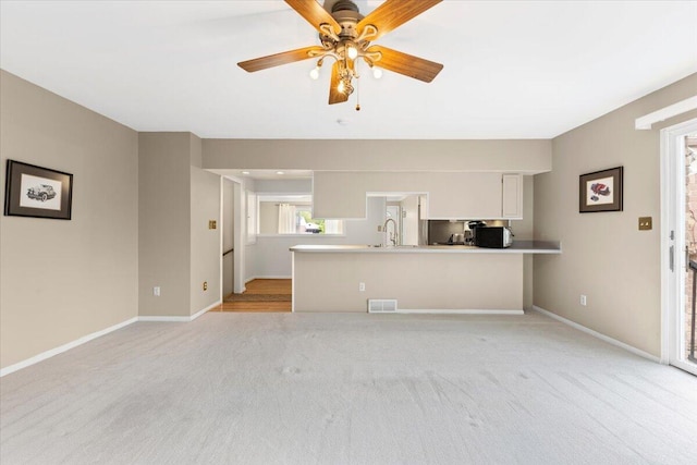 unfurnished living room with light colored carpet, a ceiling fan, baseboards, and a sink