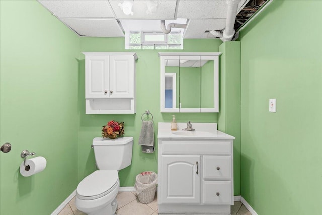 half bath with toilet, baseboards, tile patterned flooring, vanity, and a paneled ceiling