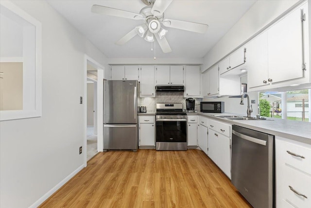 kitchen featuring appliances with stainless steel finishes, a sink, under cabinet range hood, light countertops, and tasteful backsplash