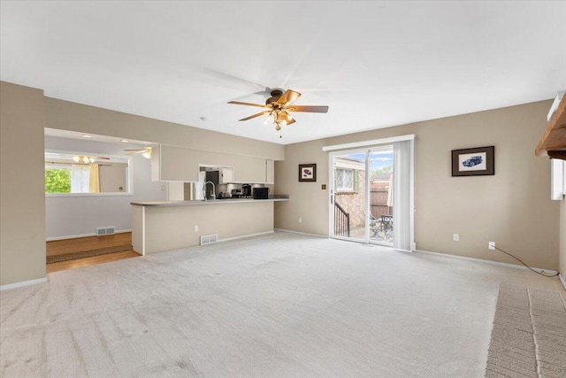 unfurnished living room with ceiling fan, light colored carpet, healthy amount of natural light, and baseboards