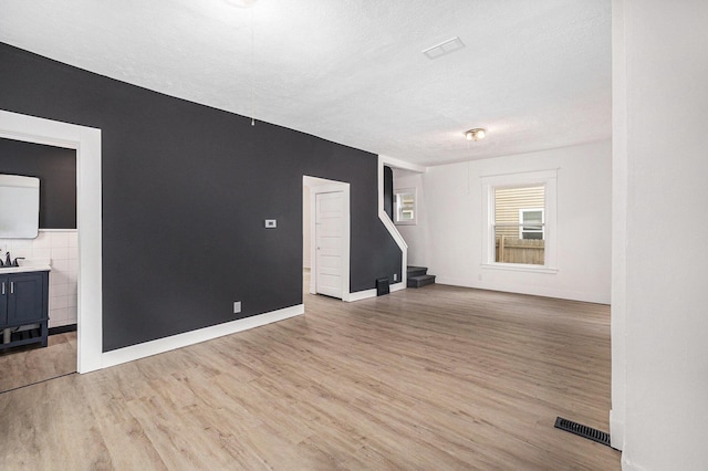 2145 Horton Ave SE, Grand Rapids, MI 49507 - unfurnished living room with light wood-style floors, stairs, a textured ceiling, and baseboards