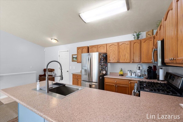 kitchen featuring appliances with stainless steel finishes, a sink, light countertops, brown cabinets, and a peninsula