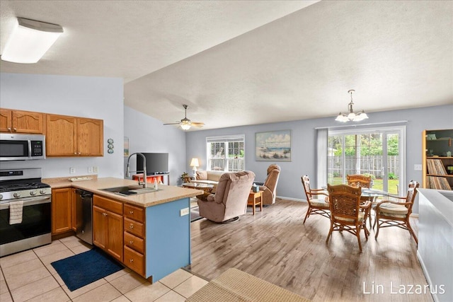 kitchen with stainless steel appliances, open floor plan, a sink, light countertops, and a peninsula