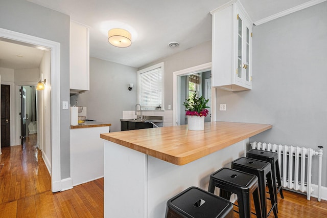 1950 Robinson Rd SE, East Grand Rapids, MI 49506 - kitchen with radiator, wood counters, wood finished floors, white cabinetry, and glass insert cabinets