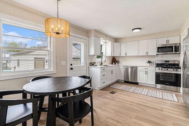 kitchen with stainless steel appliances, tasteful backsplash, light wood finished floors, light countertops, and a chandelier