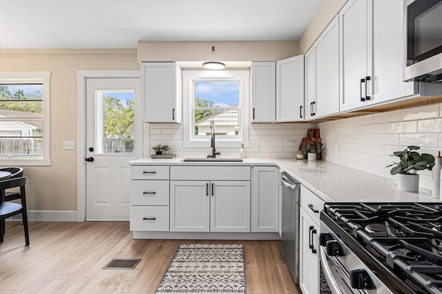 kitchen with stainless steel appliances, a sink, backsplash, light wood-type flooring, and baseboards