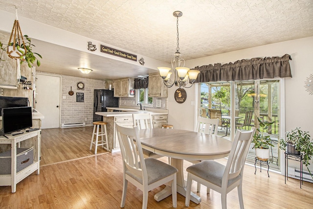 dining area with a chandelier, light wood finished floors, plenty of natural light, a baseboard heating unit, and brick wall