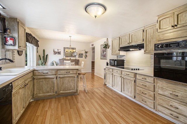 kitchen with black appliances, a sink, under cabinet range hood, a peninsula, and light wood-style floors