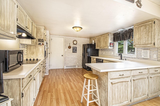 kitchen with black appliances, under cabinet range hood, light countertops, a peninsula, and a sink