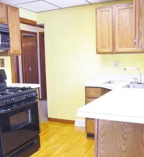 kitchen featuring black range with gas cooktop, a sink, light countertops, light wood-style flooring, and baseboards