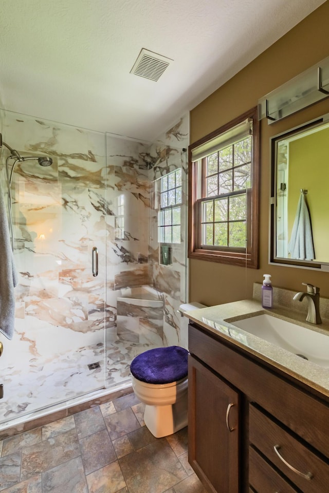 full bath with toilet, vanity, a marble finish shower, and stone finish flooring
