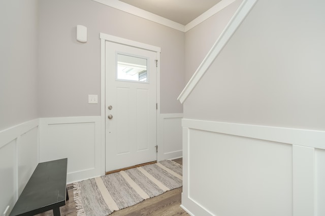 foyer entrance featuring wainscoting, wood finished floors, crown molding, and a decorative wall