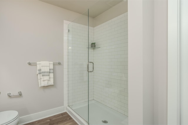 full bathroom with a stall shower, wood finished floors, baseboards, and toilet