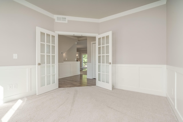 empty room with french doors, carpet, a decorative wall, a wainscoted wall, and ornamental molding