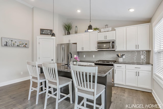 12745 Riverton Rd, Grand Haven, MI 49417 - kitchen with appliances with stainless steel finishes, lofted ceiling, backsplash, light wood-type flooring, and a kitchen island with sink
