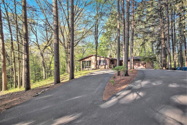 view of front of house featuring asphalt driveway, a chimney, brick siding, and a garage