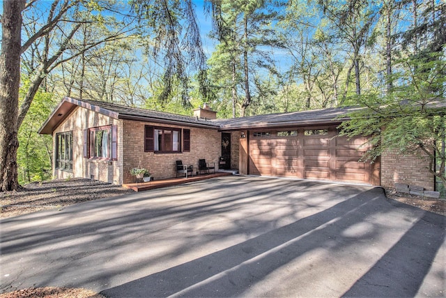 view of front of house with asphalt driveway, brick siding, a chimney, and a garage