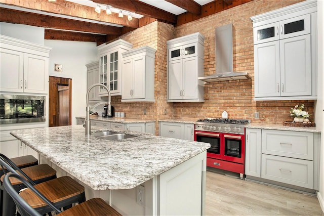 kitchen with wall chimney range hood, a sink, beamed ceiling, light wood-style floors, and stainless steel appliances